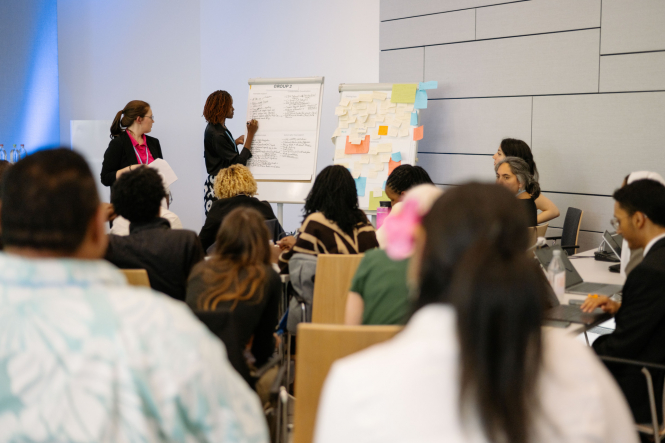 A woman writes on a white board as a room full of delegates looks on.