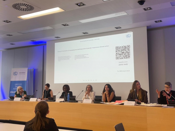 Panel of seven people seated at a long table in a conference room with a projected slide behind them and a QR code visible on the screen.