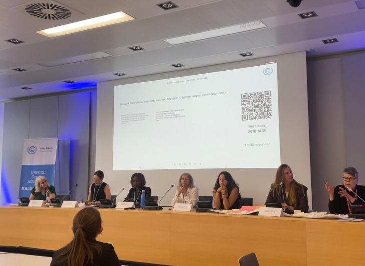 Panel of seven people seated at a long table in a conference room with a projected slide behind them and a QR code visible on the screen.