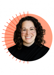 Smiling woman with curly brown hair, wearing a black turtleneck, portrait against a peach circular background with orange sunburst rays.